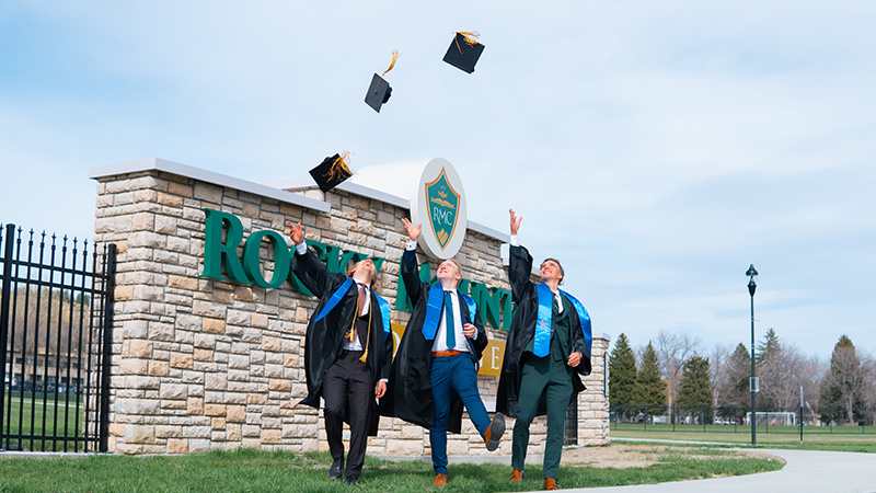 Outdoor image of three male graduates tossing their mortarboards up